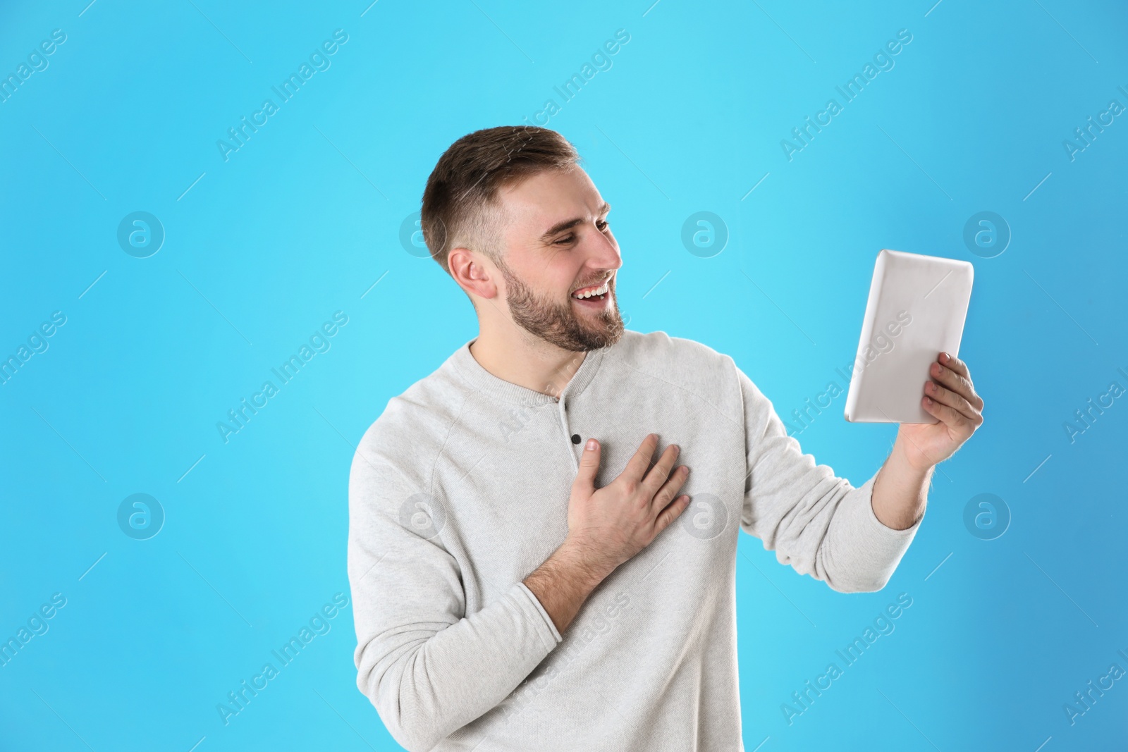 Photo of Young man using video chat on tablet against color background