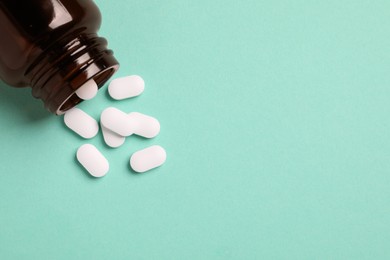 Photo of Plastic medical bottle with pills on turquoise background, flat lay. Space for text