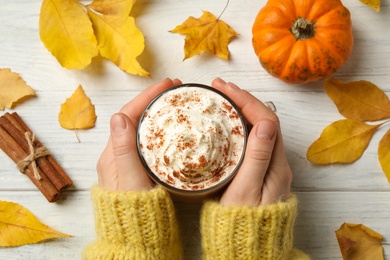 Photo of Woman holding tasty pumpkin latte at white wooden table, top view