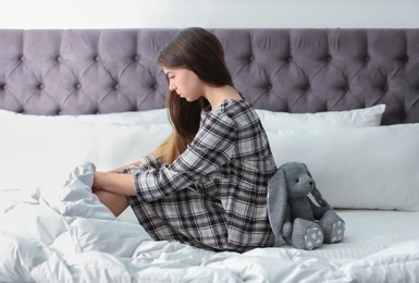 Upset teenage girl with toy sitting on bed