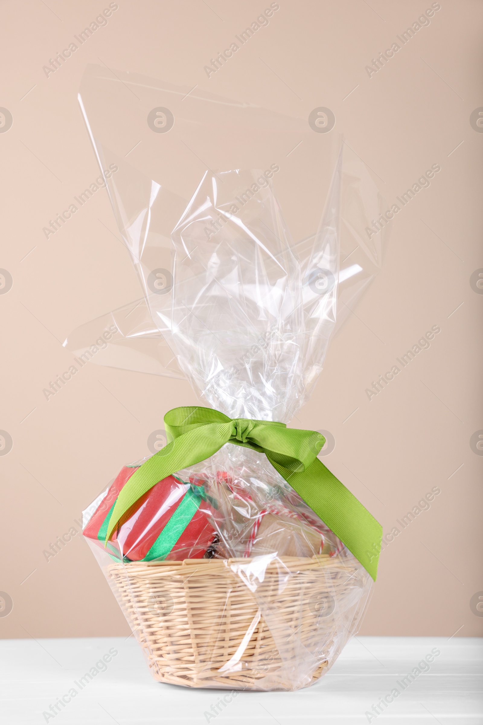 Photo of Wicker basket full of gift boxes on white wooden table against beige background