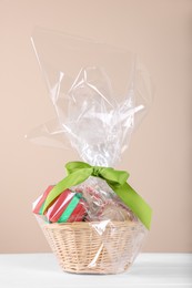 Photo of Wicker basket full of gift boxes on white wooden table against beige background