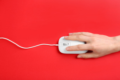 Woman using modern wired optical mouse on red background, top view