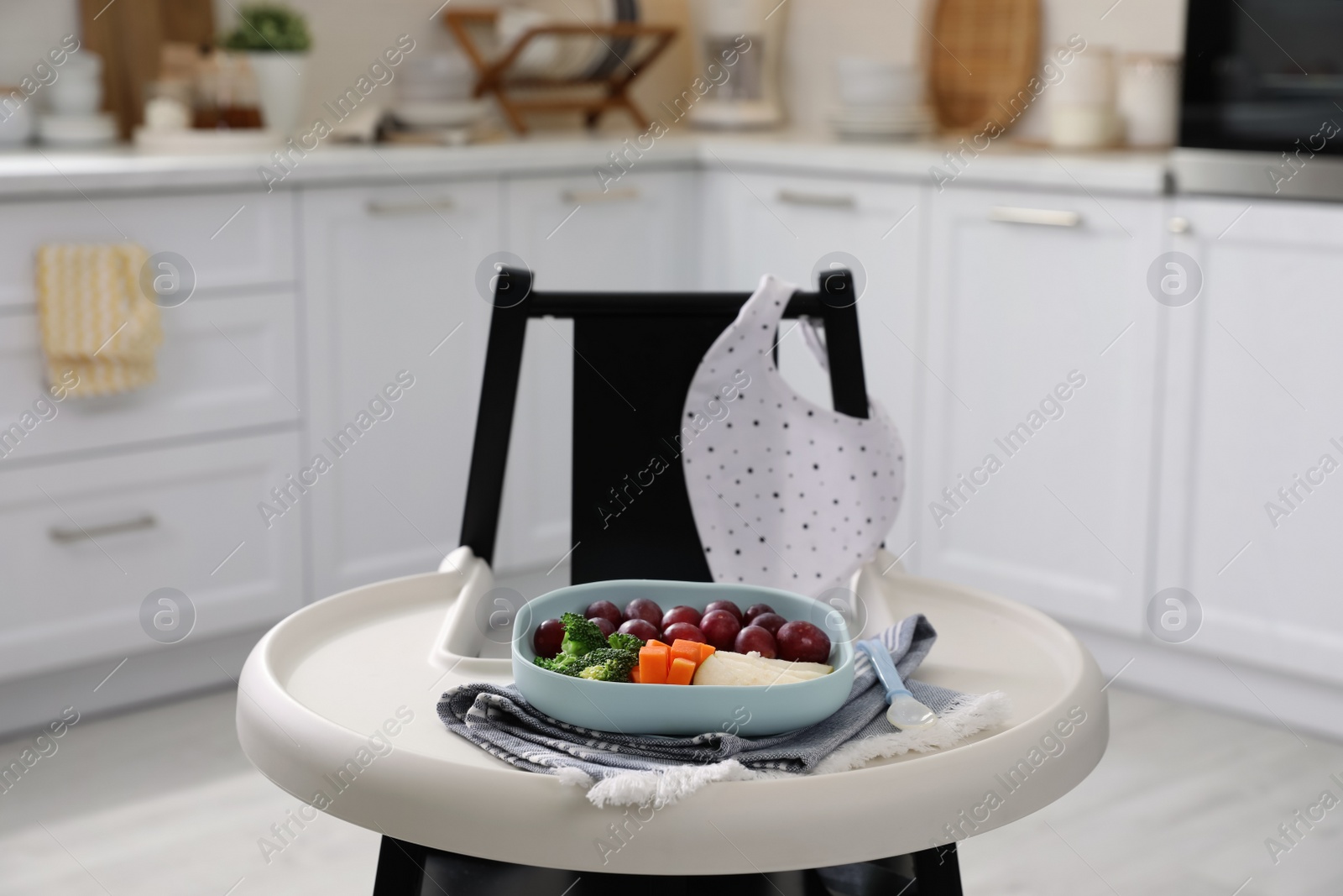 Photo of High chair with food in baby tableware on tray indoors