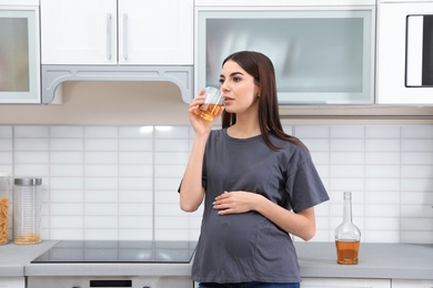 Photo of Future mother drinking alcohol in kitchen. Bad habits during pregnancy