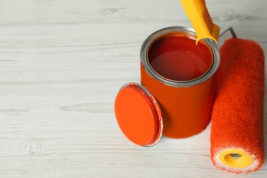 Photo of Can of orange paint and roller on white wooden table. Space for text