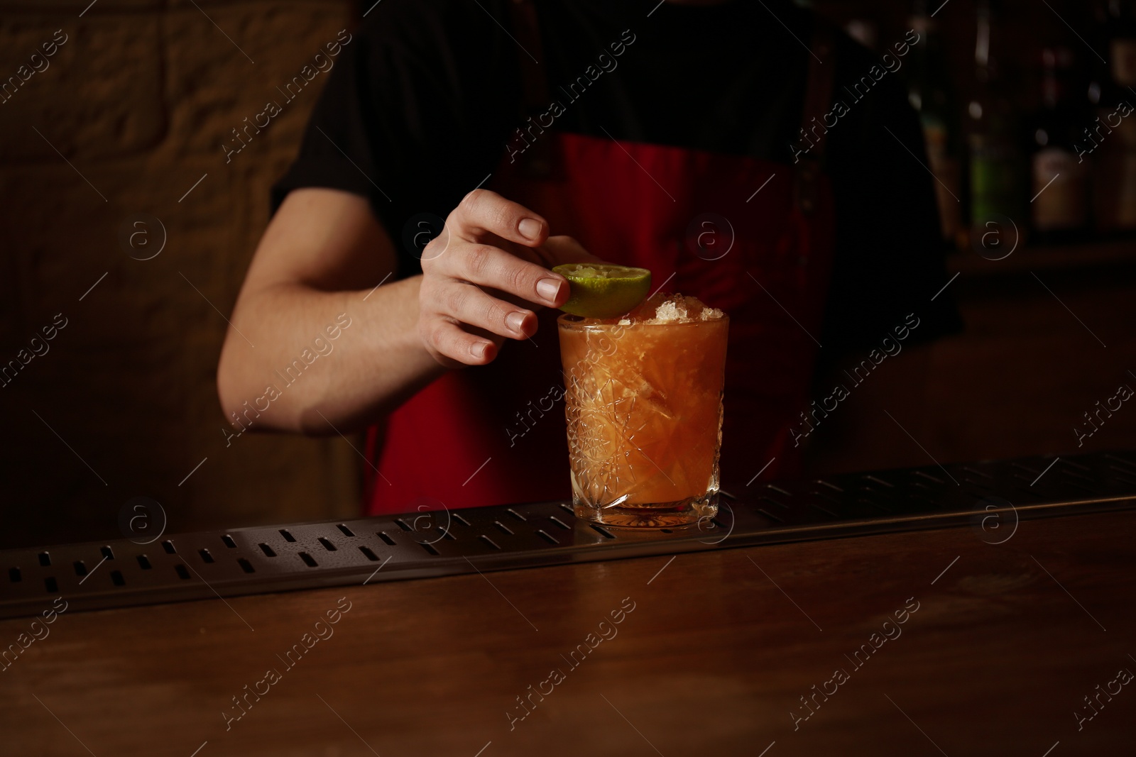 Photo of Bartender decorating glass of fresh alcoholic cocktail at bar counter, closeup