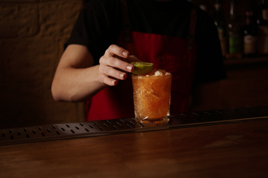 Bartender decorating glass of fresh alcoholic cocktail at bar counter, closeup