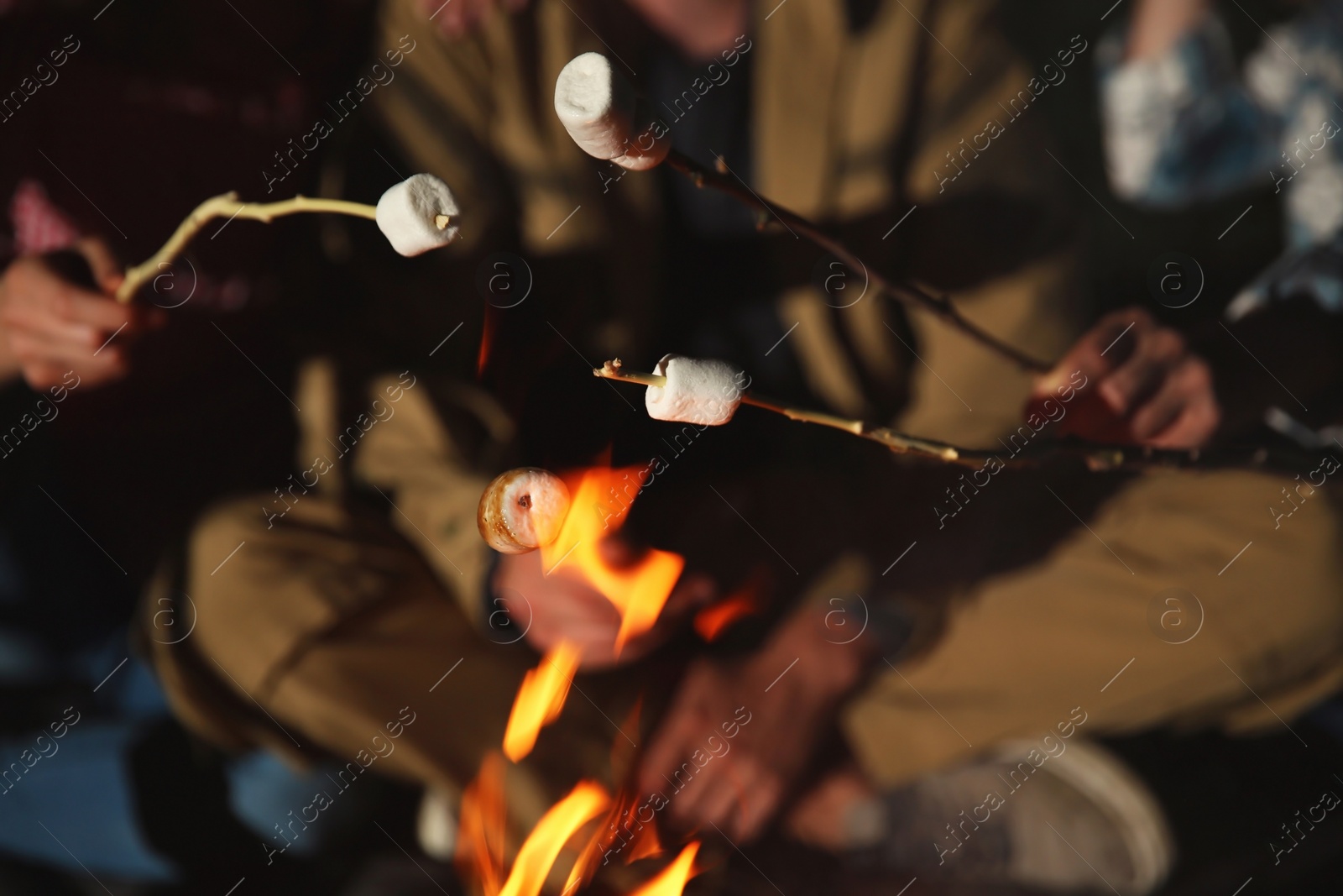 Photo of Friends frying marshmallows on bonfire at night, closeup. Camping season