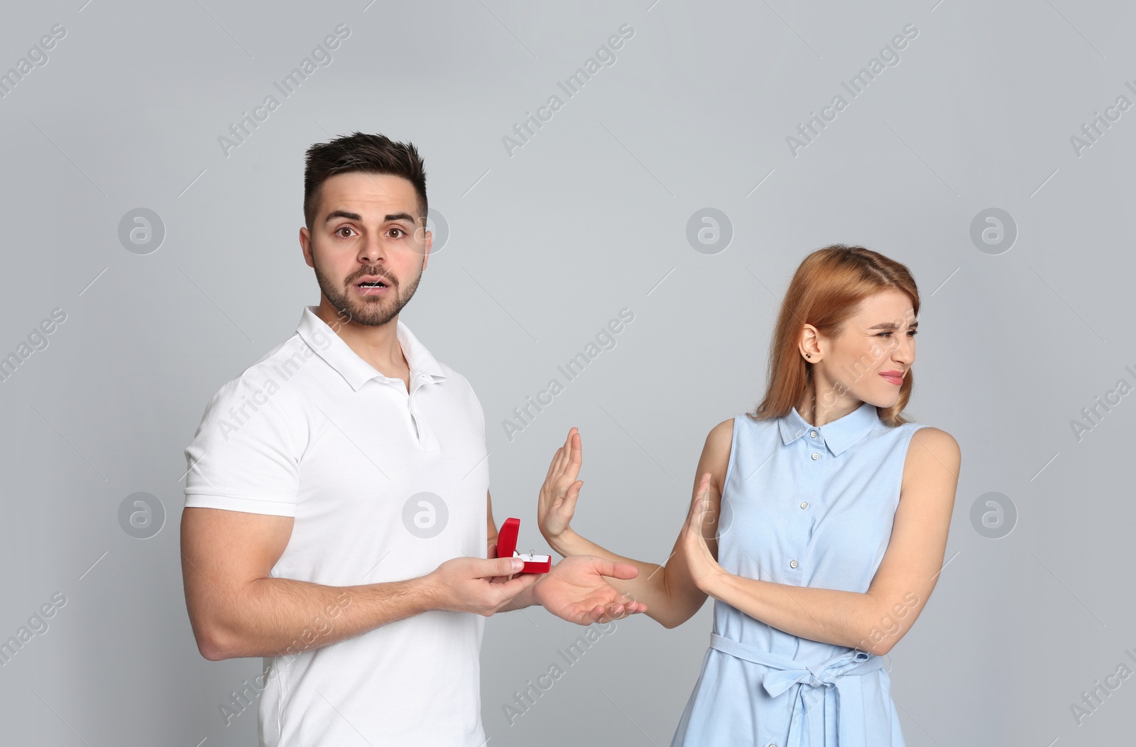 Photo of Young woman rejecting engagement ring from boyfriend on light grey background