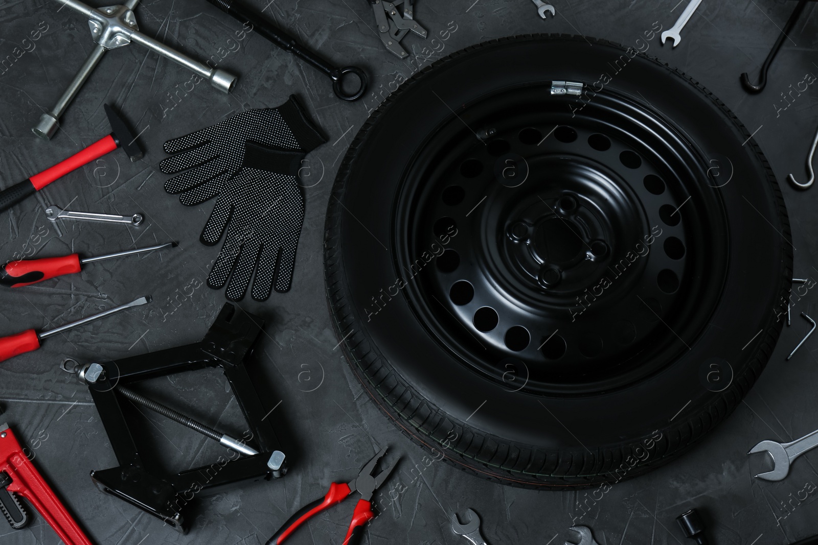 Photo of Car wheel, scissor jack and different tools on dark grey surface, flat lay