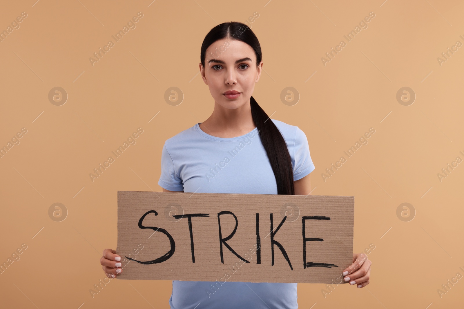Photo of Woman holding cardboard banner with word Strike on beige background