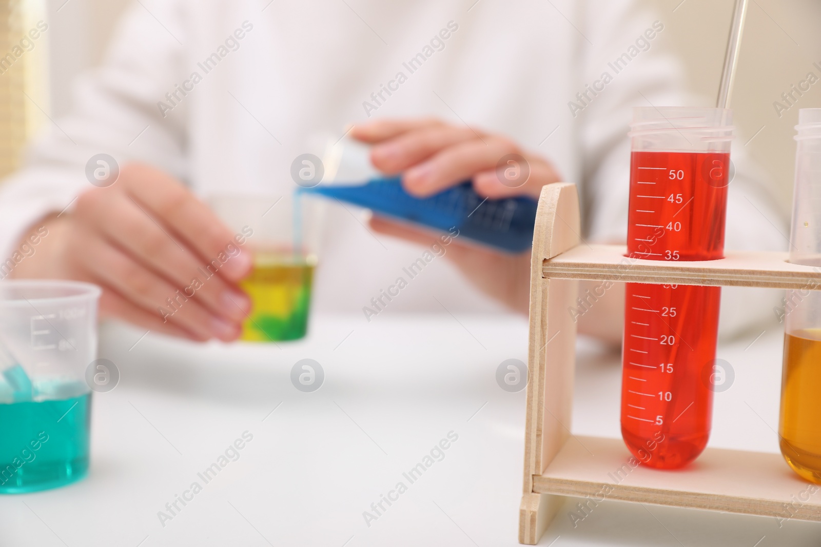 Photo of Girl mixing colorful liquids at white table indoors, selective focus. Kids chemical experiment set