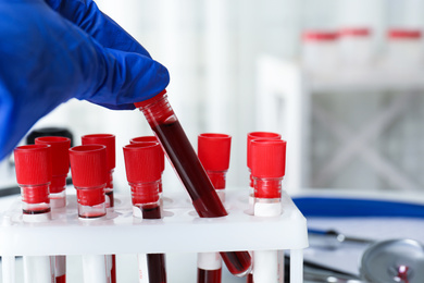 Photo of Scientist taking test tube with blood sample from rack in laboratory, closeup. Virus research