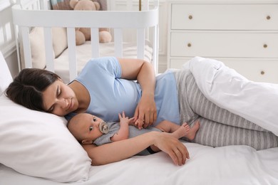 Photo of Tired young mother sleeping with her baby in bed at home