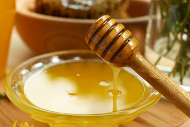 Photo of Delicious honey flowing down from dipper into bowl on wooden table, closeup