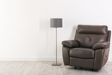 Comfortable armchair and lamp near wall with space for design. Stylish interior elements