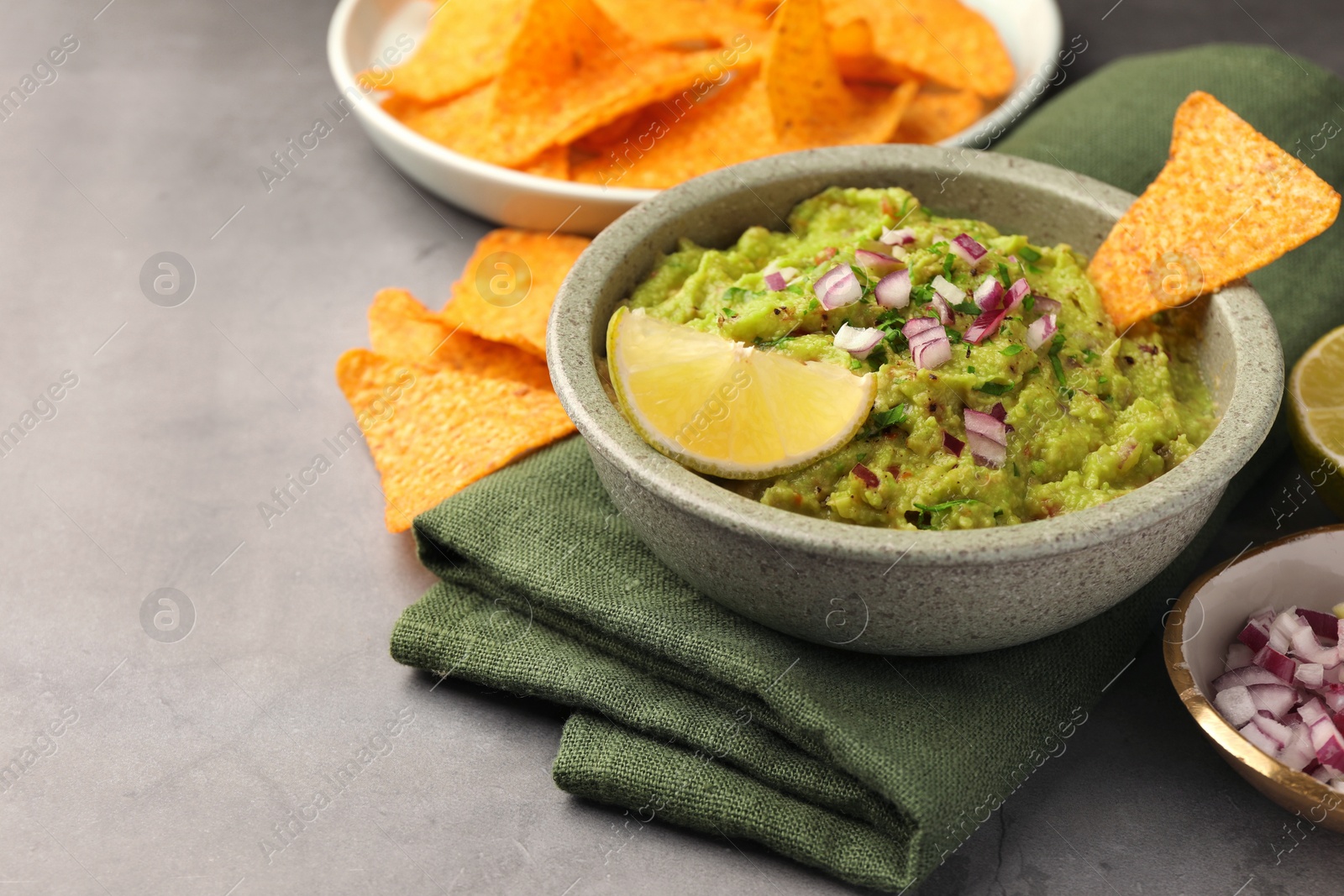 Photo of Bowl of delicious guacamole, nachos chips and lime on grey table, closeup. Space for text