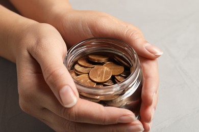 Woman holding glass jar with coins on light grey background, closeup