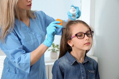 Doctor using nit comb and spray on girl's hair indoors. Anti lice treatment