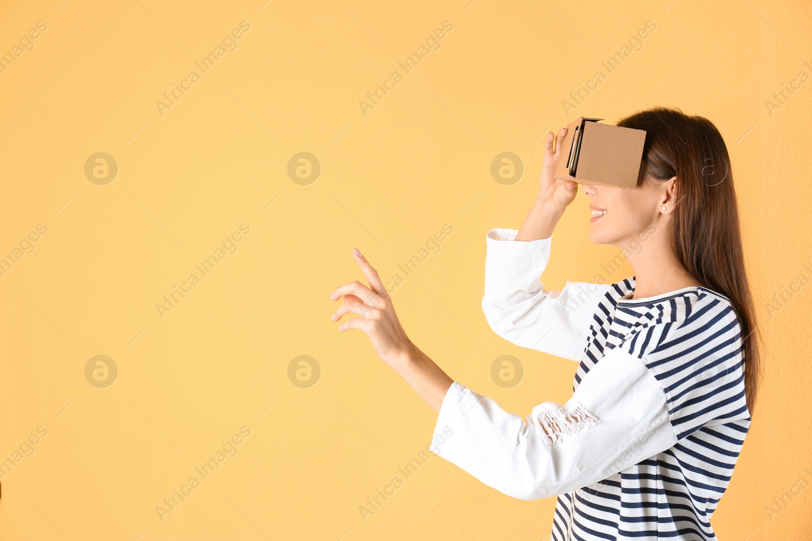 Photo of Young woman using cardboard virtual reality headset on color background. Space for text