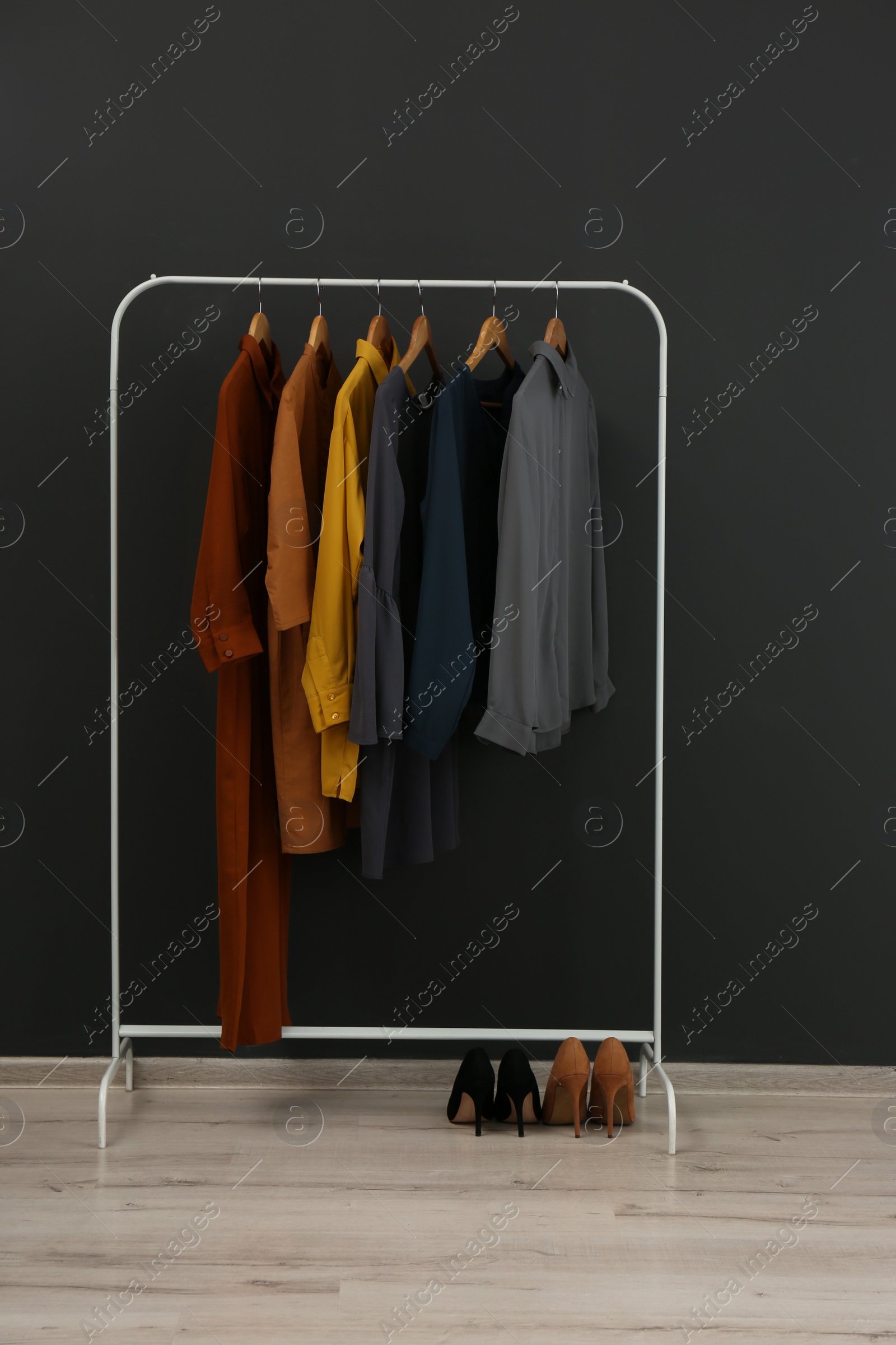 Photo of Rack with stylish clothes near black wall