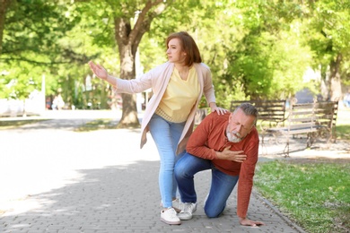 Woman helping mature man suffering from heart attack in park