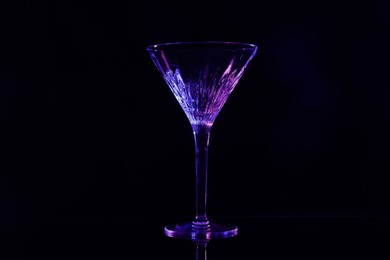 Beautiful martini glass on mirror table against black background