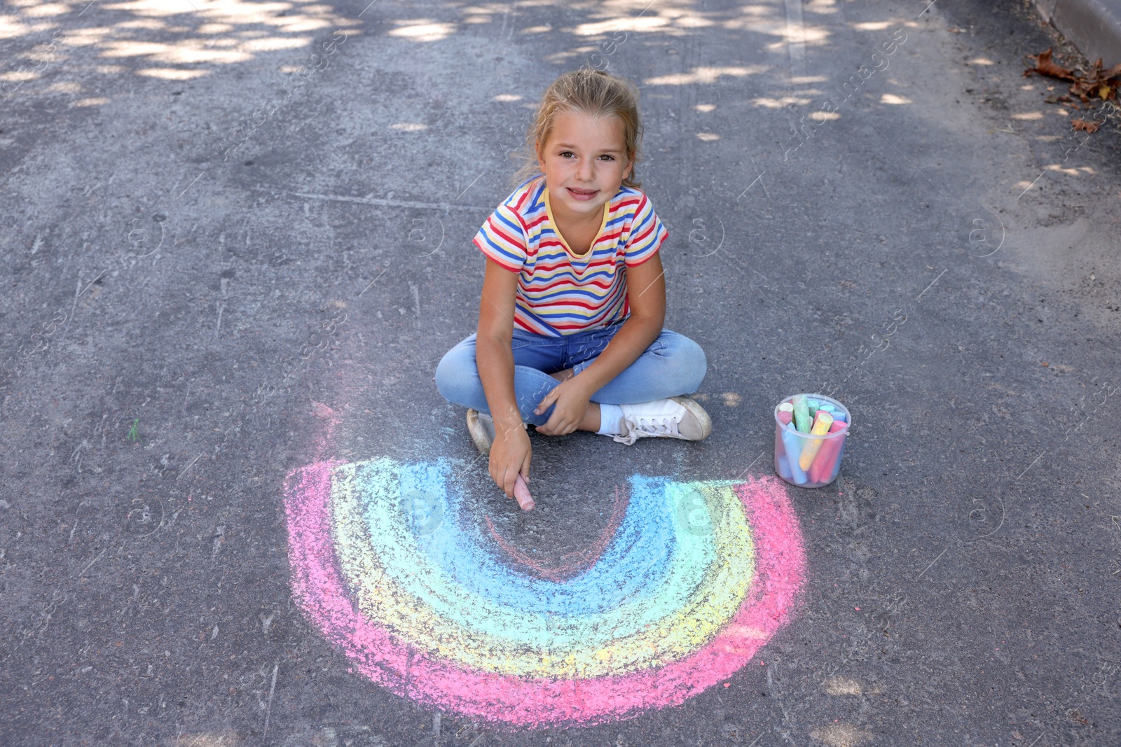 Photo of Cute little child drawing rainbow with colorful chalk on asphalt