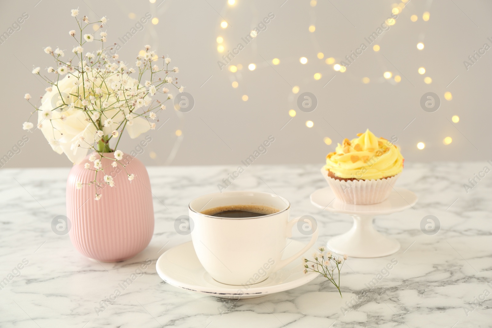 Photo of Delicious cupcake with yellow cream, coffee and flowers on white marble table