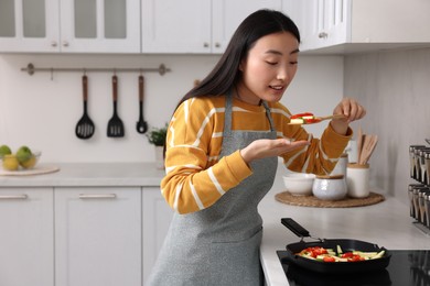 Photo of Beautiful woman cooking and tasting vegetable dish in kitchen. Space for text