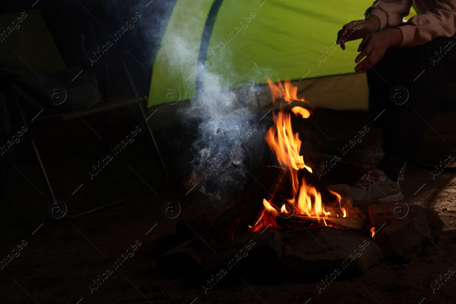 Photo of Woman sitting near bonfire and camping tent at night