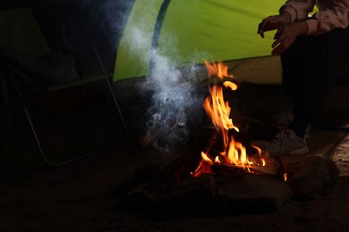 Woman sitting near bonfire and camping tent at night