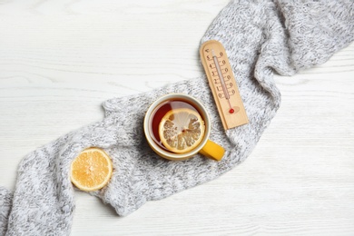 Flat lay composition with thermometer, cup of tea, lemon and knitted scarf on white wooden background