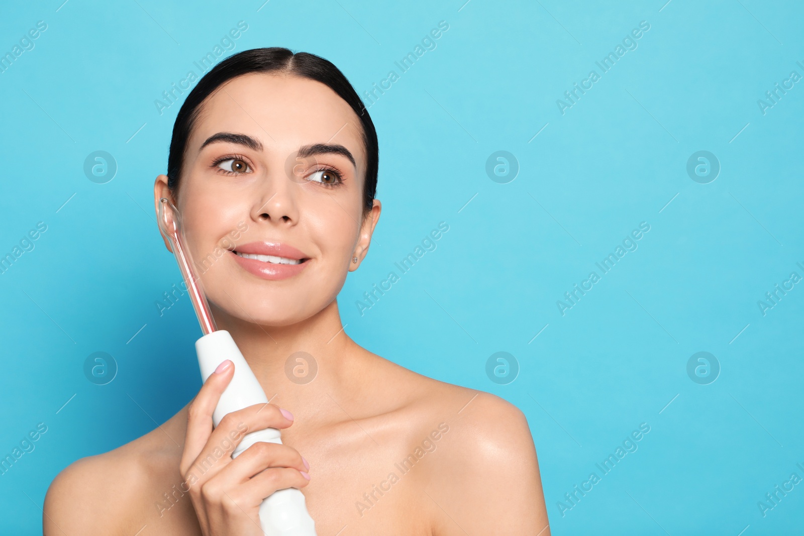 Photo of Woman using high frequency darsonval device on light blue background. Space for text