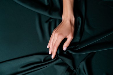 Photo of Woman touching soft dark green fabric, top view