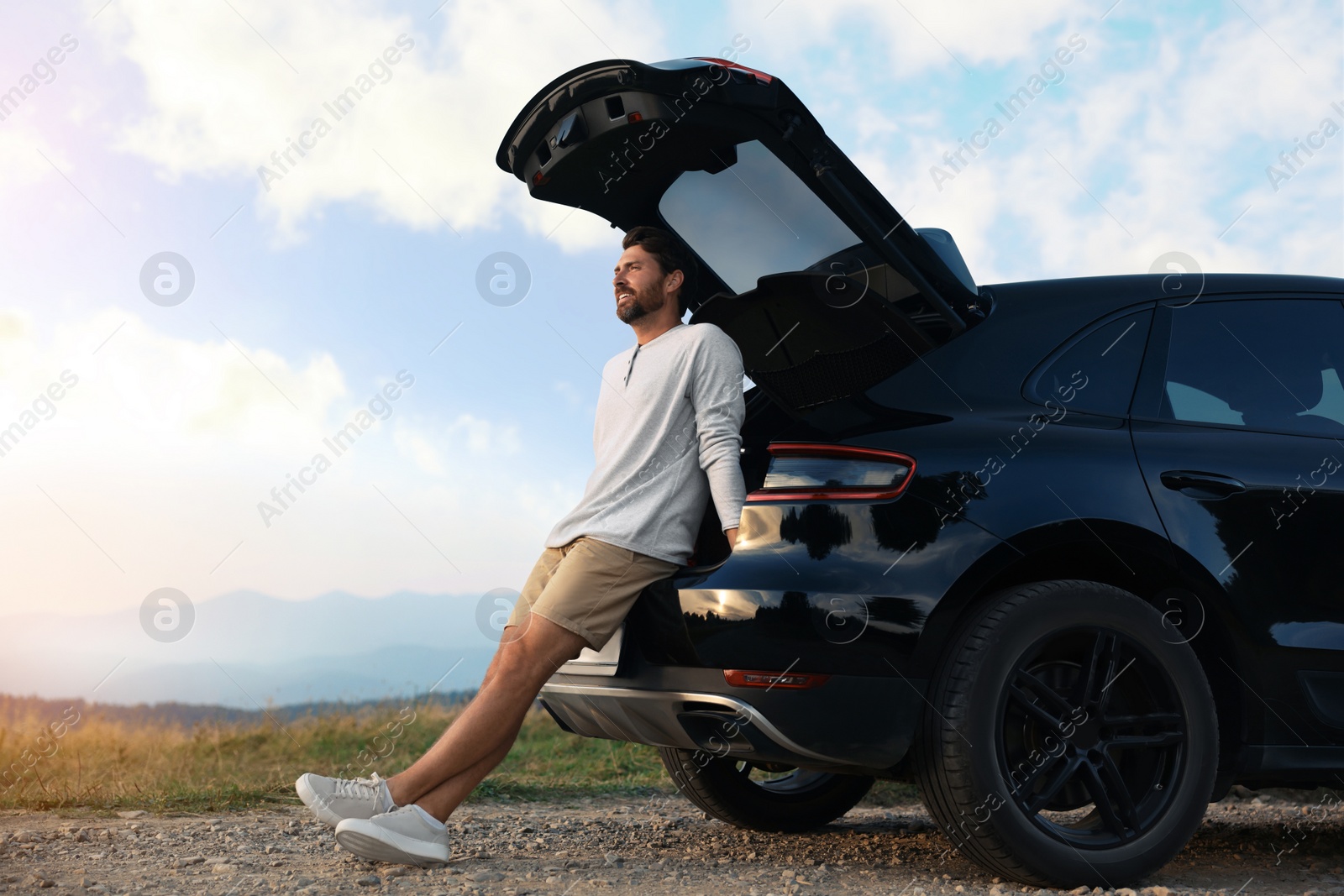 Photo of Happy man sitting in trunk of modern car on roadside outdoors