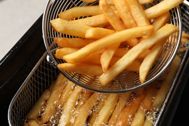 Photo of Delicious freshly prepared french fries in metal strainer, closeup