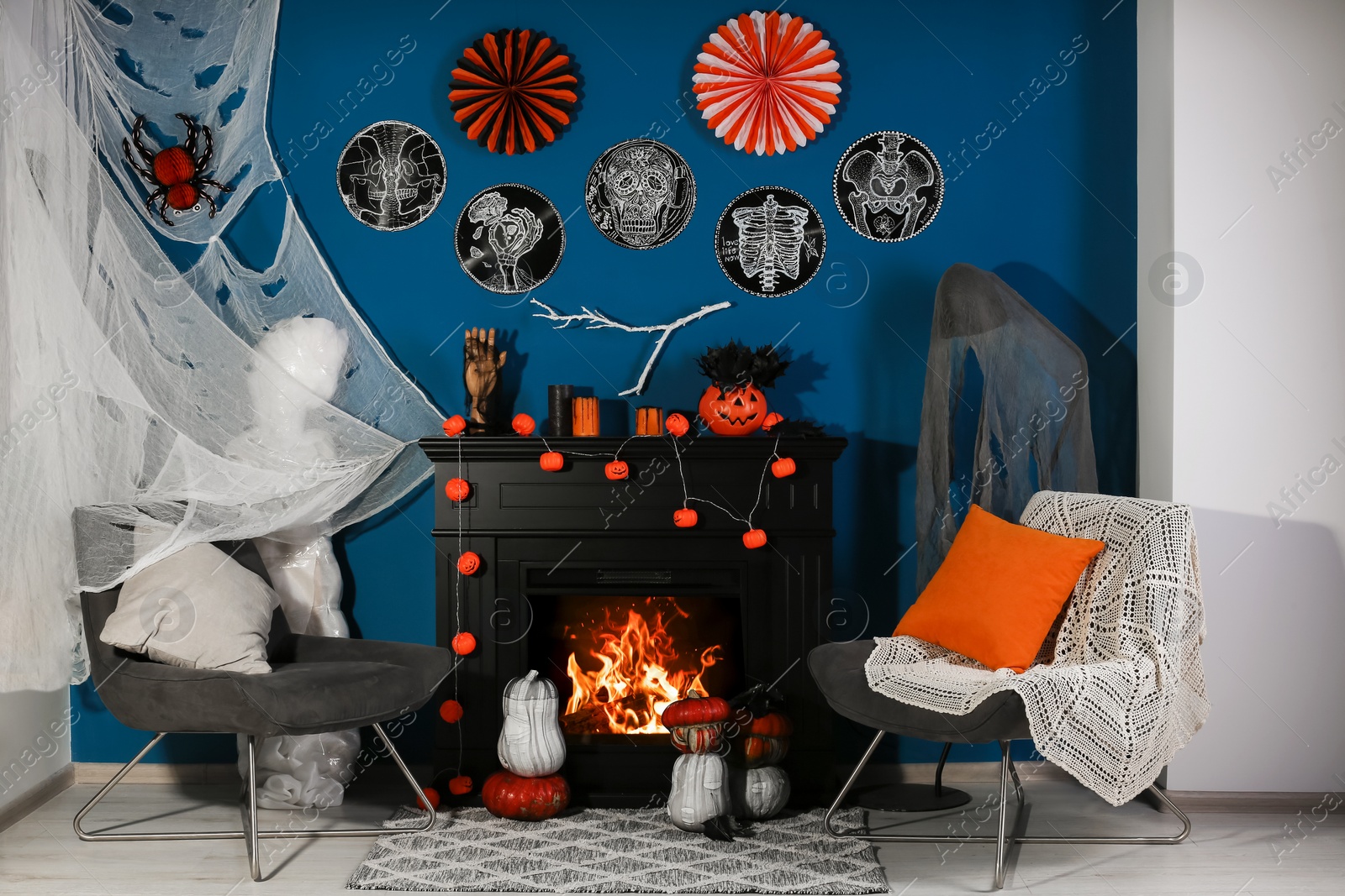 Photo of Jack-o'-lanterns and different Halloween decorations on black fireplace near blue wall