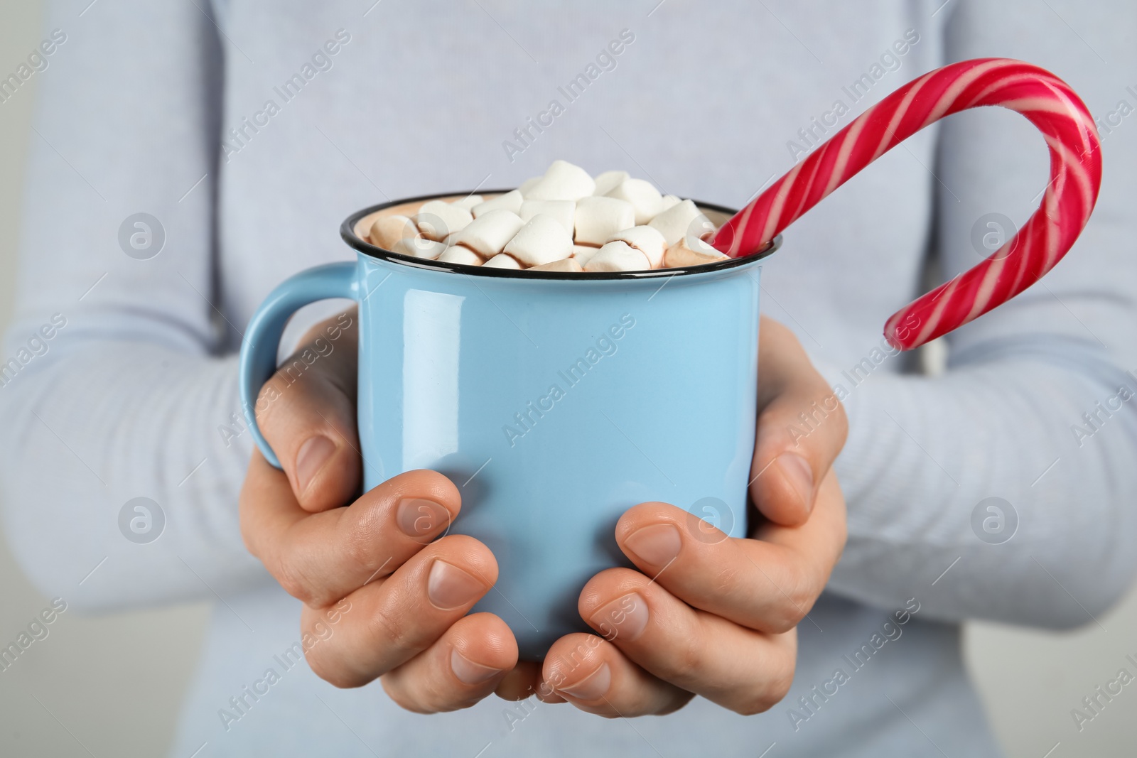 Photo of Woman holding cup of delicious hot chocolate with marshmallows and candy cane, closeup