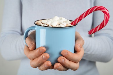 Woman holding cup of delicious hot chocolate with marshmallows and candy cane, closeup