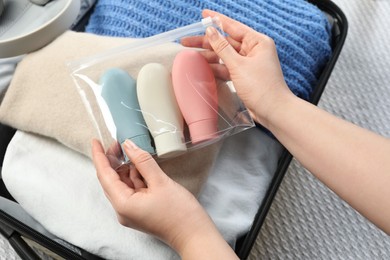 Photo of Woman with plastic bag of cosmetic travel kit packing suitcase, top view