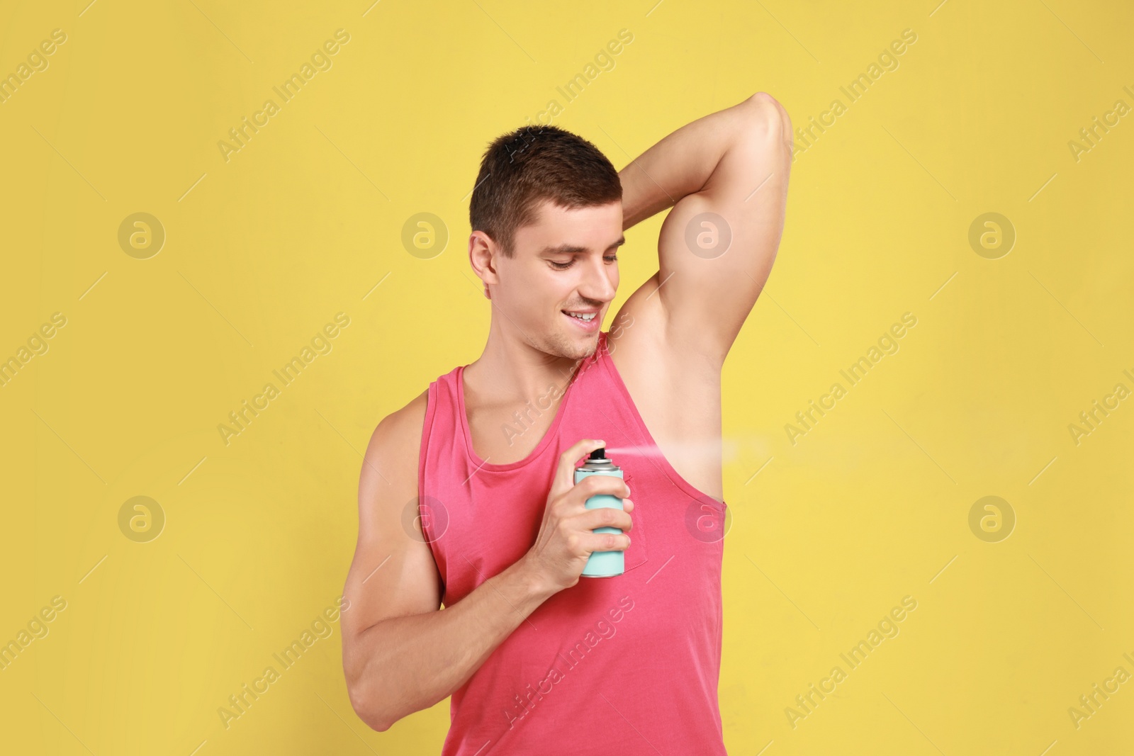 Photo of Young man applying deodorant to armpit on yellow background