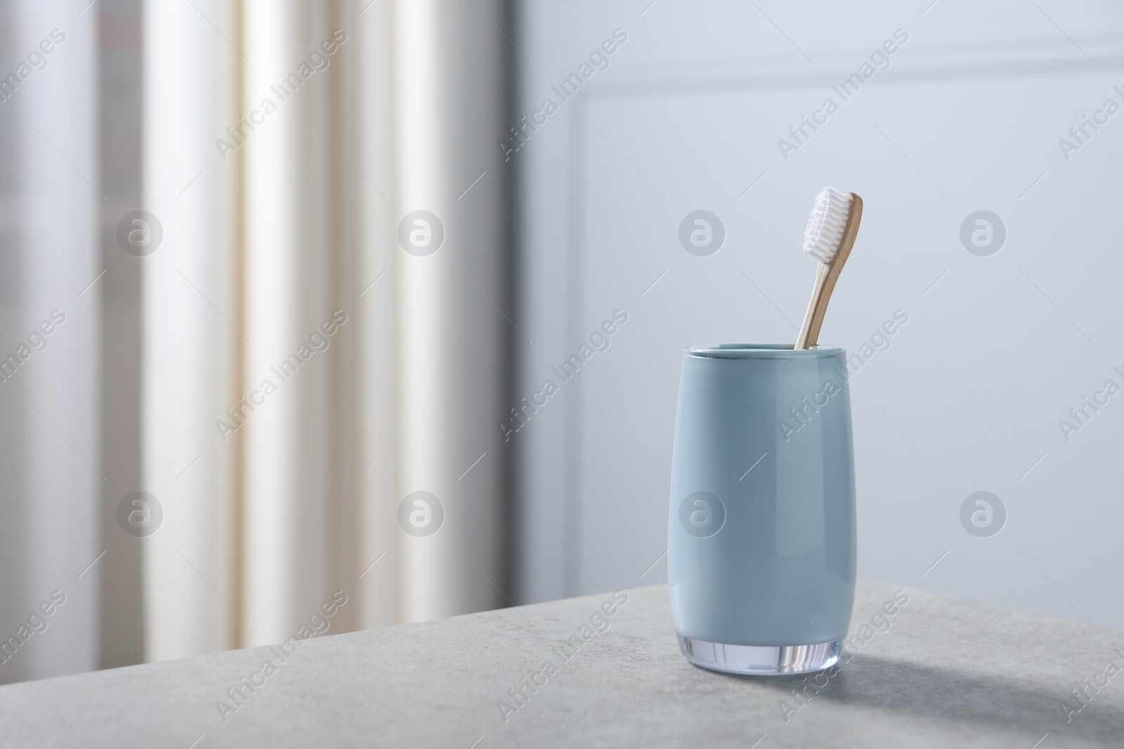 Photo of Bamboo toothbrush in holder on light grey table indoors. Space for text