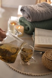 Photo of Pouring freshly brewed tea into cup at table in room, closeup. Cozy home atmosphere