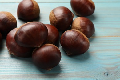 Photo of Roasted edible sweet chestnuts on light blue wooden table, closeup