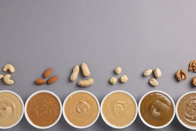 Photo of Many tasty nut butters in bowls and nuts on grey table, flat lay. Space for text