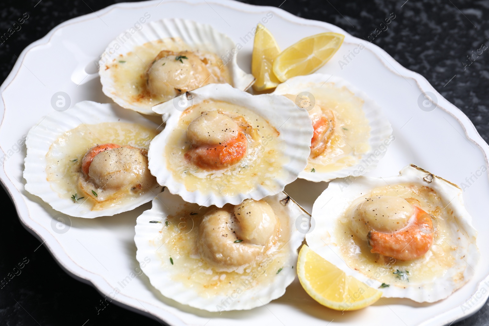 Photo of Fried scallops in shells and lemon on black textured table, closeup