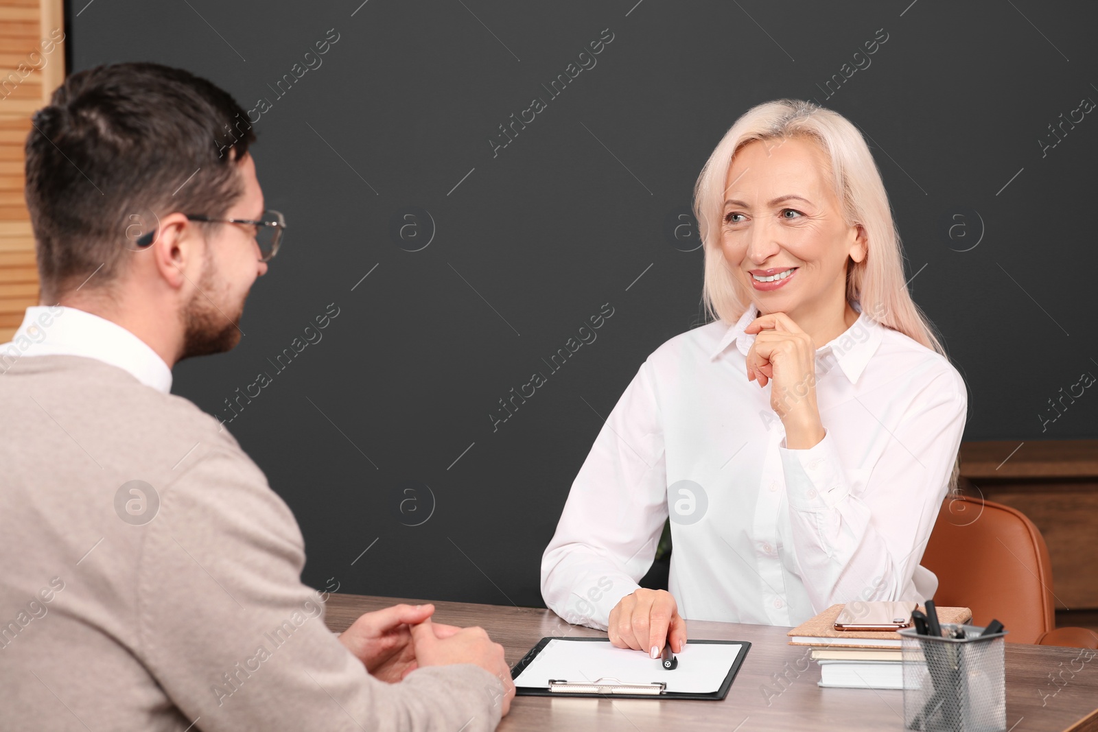 Photo of Happy woman having conversation with man at wooden table in office. Manager conducting job interview with applicant