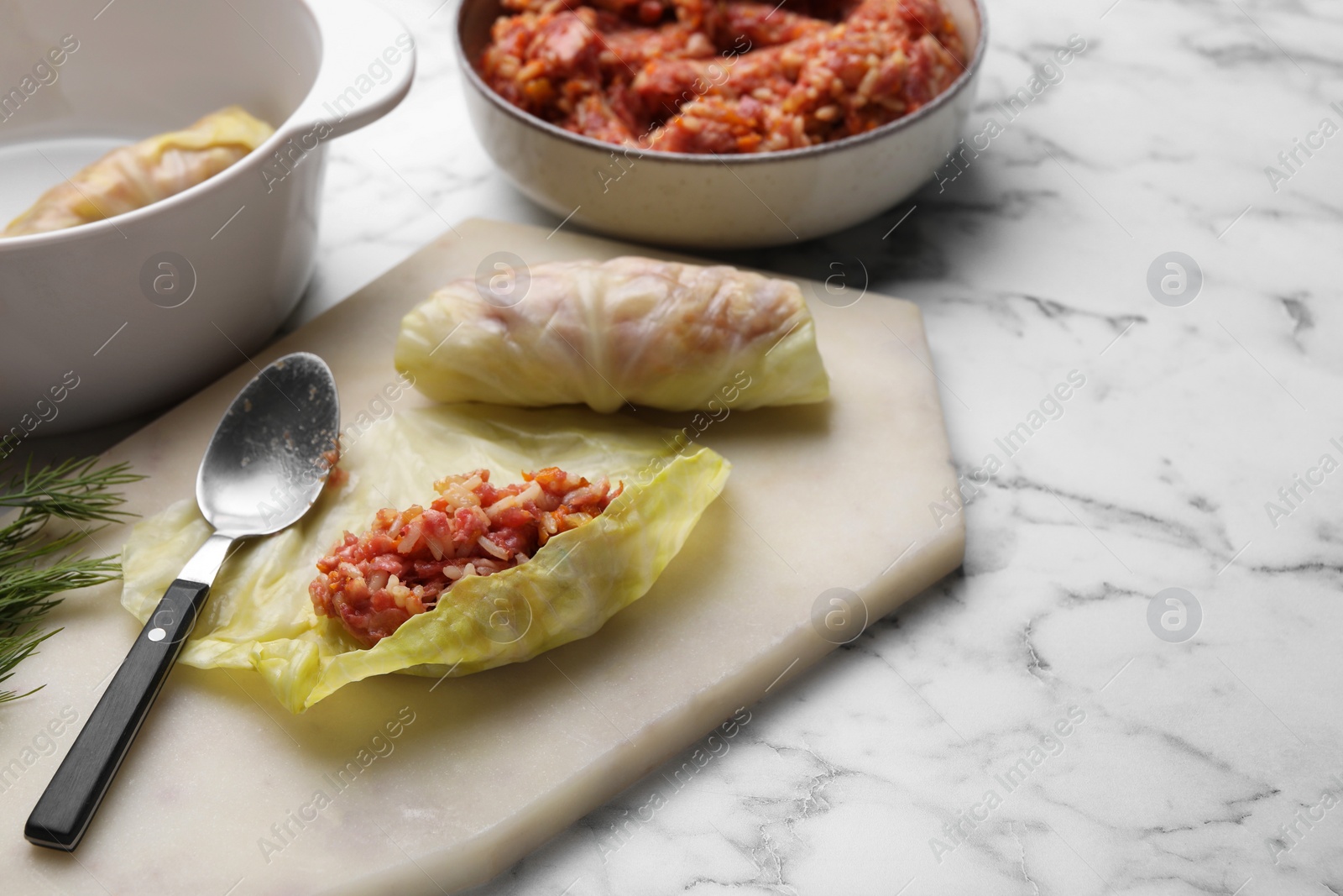 Photo of Preparing stuffed cabbage rolls on white marble table. Space for text